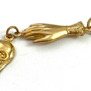 Op de afbeelding: Een gouden bedel met een gedetailleerde schedel en een hand met een manchet. De bedel is bevestigd aan een gouden ring.
