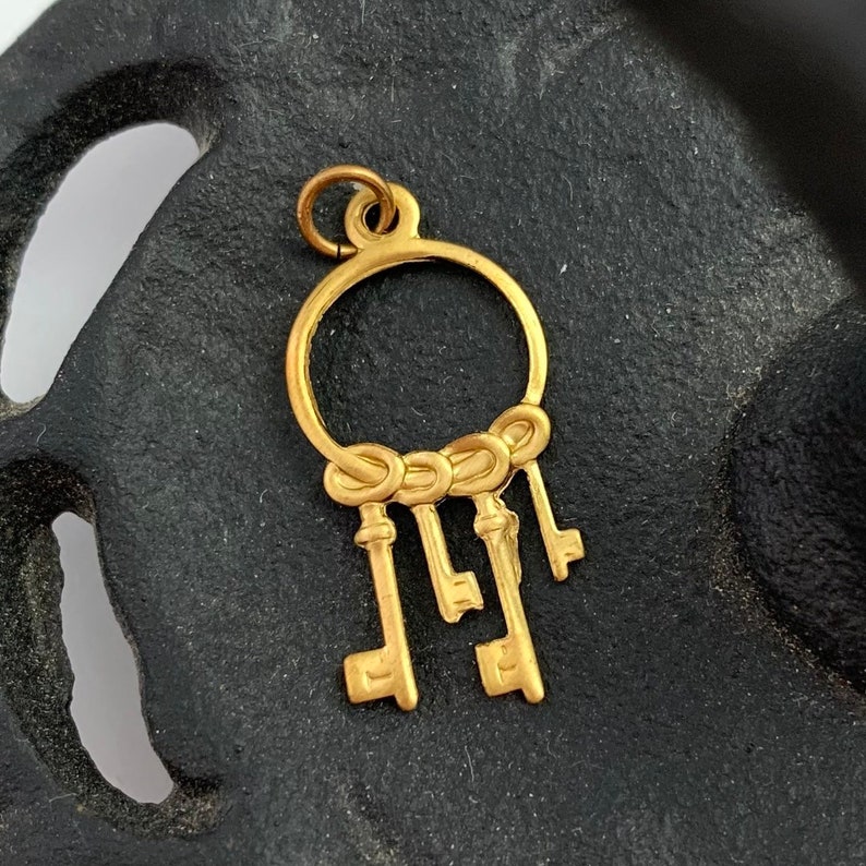 Op de afbeelding: Gouden bedel met een cirkel waaraan vijf sleutels hangen. De sleutels zijn met een knoop aan elkaar gebonden.