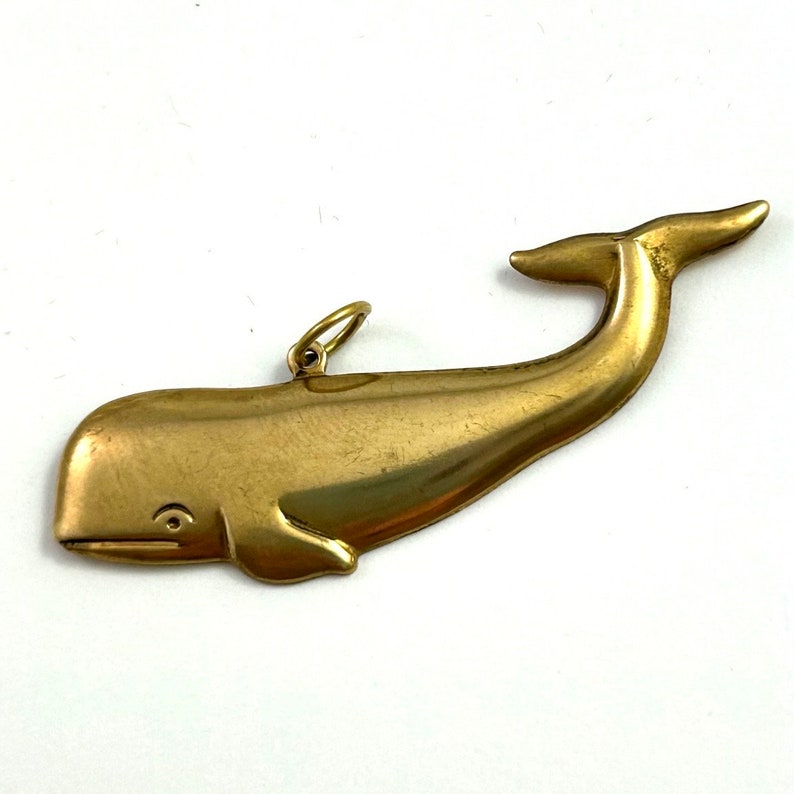 May include: A gold-coloured whale charm pendant. The whale is depicted in a stylised, simple design with a smooth, shiny finish.