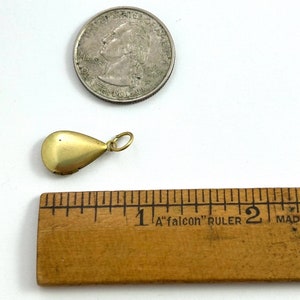 May include: A gold teardrop-shaped locket pendant with a hinged opening. The locket is about 1 inch long and is shown next to a US quarter for size comparison.