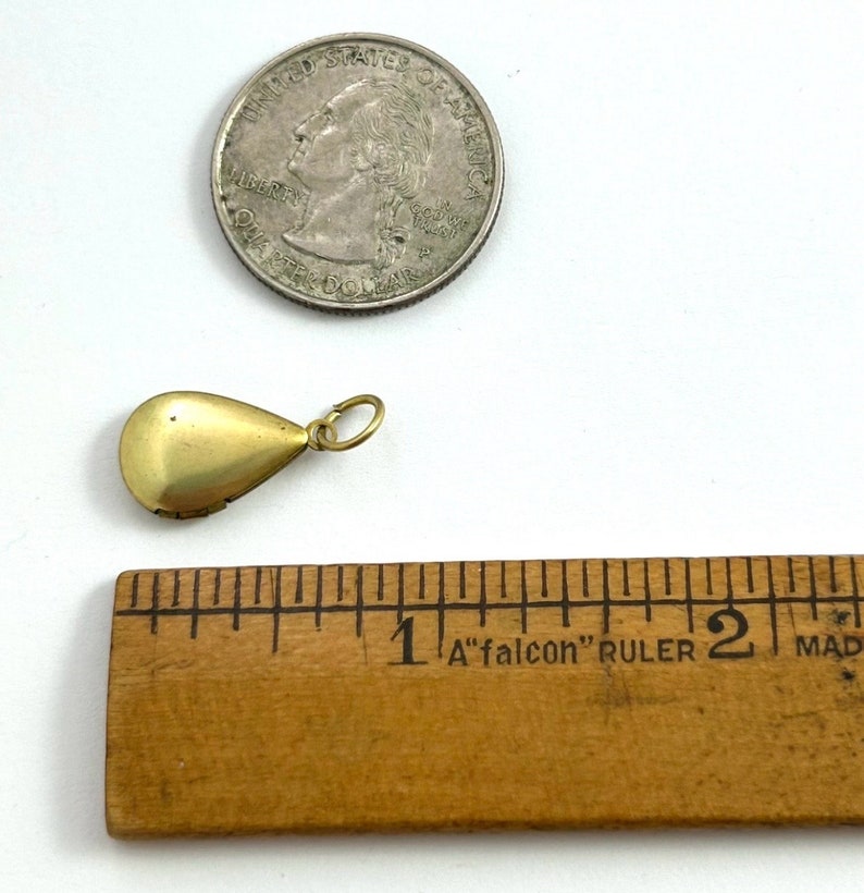 May include: A gold teardrop-shaped locket pendant with a hinged opening. The locket is about 1 inch long and is shown next to a US quarter for size comparison.