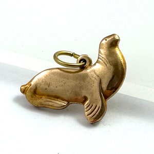 May include: A gold-colored charm in the shape of a seal. The charm has a loop at the top for attaching to a necklace or bracelet.
