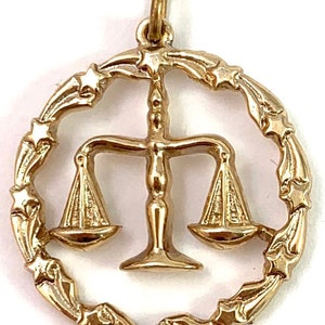 May include: Gold-tone pendant charm featuring the astrological symbol for Libra, a set of scales, surrounded by a circle of stars.
