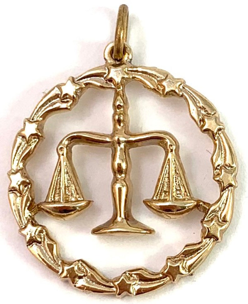 May include: Gold-tone pendant charm featuring the astrological symbol for Libra, a set of scales, surrounded by a circle of stars.