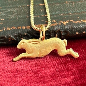 May include: A gold-coloured necklace with a detailed rabbit pendant. The rabbit is depicted in a running pose with its ears raised.