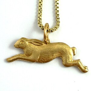 May include: A gold-toned necklace featuring a detailed, three-dimensional rabbit pendant. The rabbit is depicted in a running pose, with its ears and tail extended.