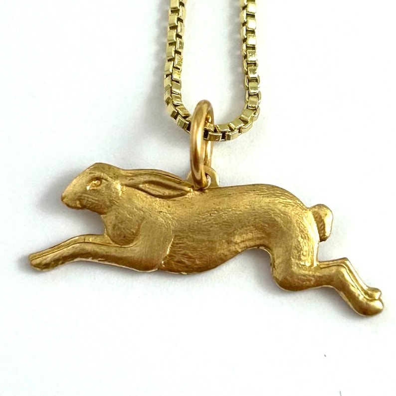 May include: A gold-toned necklace featuring a detailed, three-dimensional rabbit pendant. The rabbit is depicted in a running pose, with its ears and tail extended.
