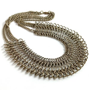 May include: A gold-toned metal necklace with a layered design. The necklace features a large, open, fan-shaped pendant made of multiple interconnected rings.
