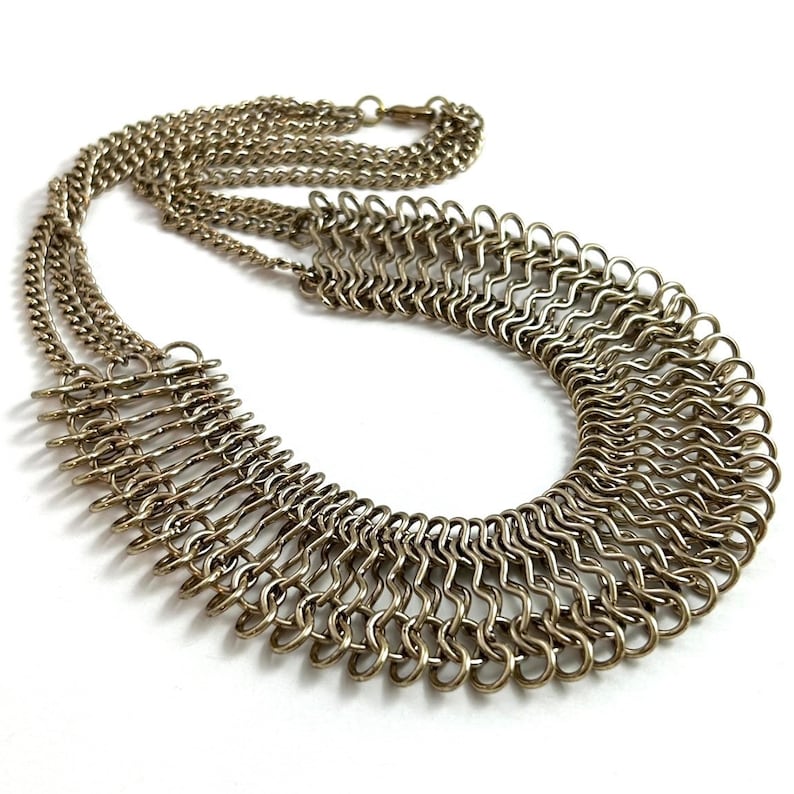 May include: A gold-toned metal necklace with a layered design. The necklace features a large, open, fan-shaped pendant made of multiple interconnected rings.