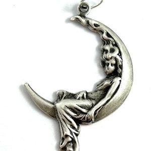 May include: A silver charm pendant featuring a woman sitting on a crescent moon. The woman is depicted in a flowing gown and has long hair. The charm is detailed and intricate.