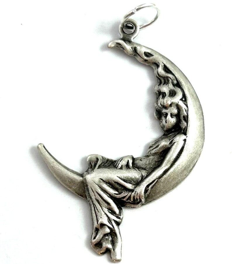 May include: A silver charm pendant featuring a woman sitting on a crescent moon. The woman is depicted in a flowing gown and has long hair. The charm is detailed and intricate.