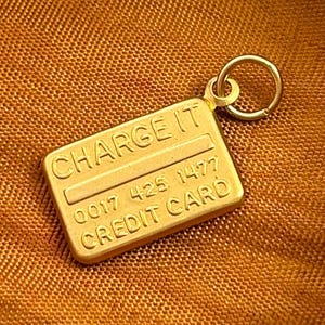May include: Gold-toned charm shaped like a credit card with the words "CHARGE IT" and "CREDIT CARD" and the numbers "0017 425 1477".