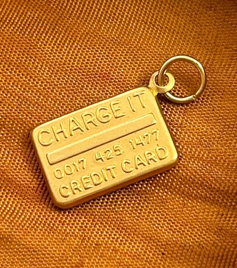 May include: Gold-toned charm shaped like a credit card with the words "CHARGE IT" and "CREDIT CARD" and the numbers "0017 425 1477".