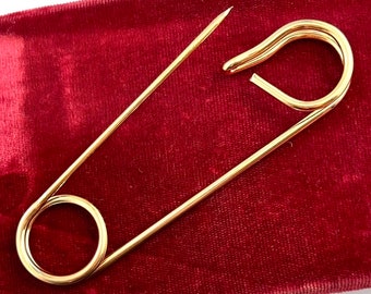 May include: A large gold safety pin on a red velvet background.