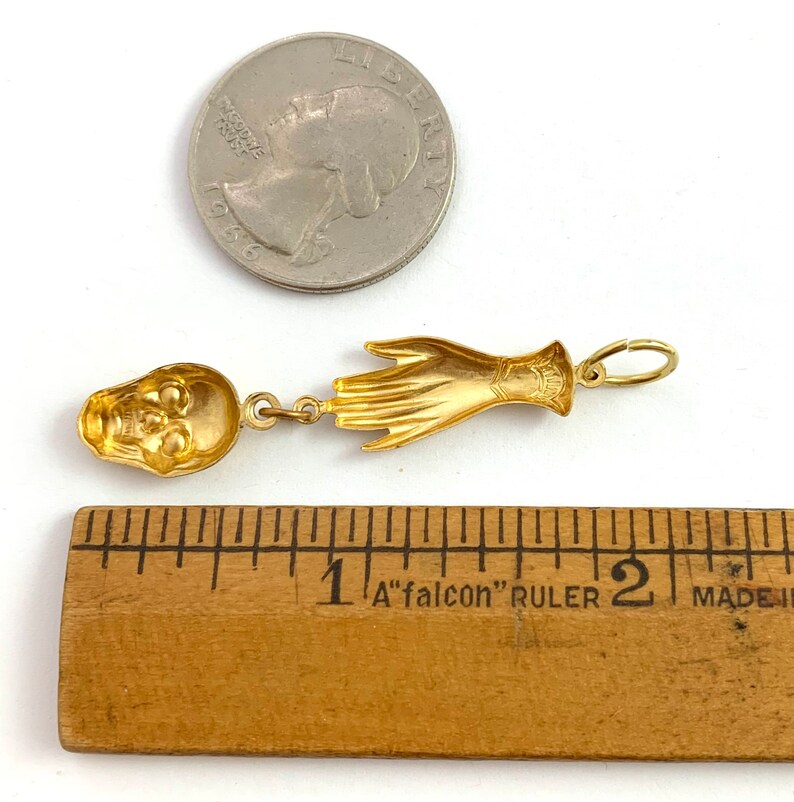 Op de afbeelding: Goudkleurige hanger met een schedel en een hand. De hanger is ongeveer 2,5 cm lang.