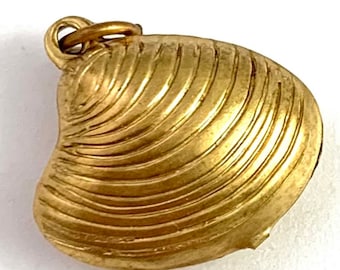 Puede incluir: Un colgante de concha de mar de metal dorado. La concha está detallada con un diseño texturizado y acanalado.