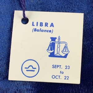 May include: A white tag with blue text and a blue illustration of a scale. The tag says "LIBRA (Balance)" and "SEPT. 23 to OCT. 22".