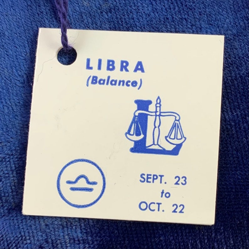 May include: A white tag with blue text and a blue illustration of a scale. The tag says "LIBRA (Balance)" and "SEPT. 23 to OCT. 22".