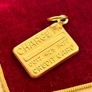 May include: Gold-coloured charm shaped like a credit card with the words "CHARGE IT" and "CREDIT CARD" and the number "0017 425 1477" on it.