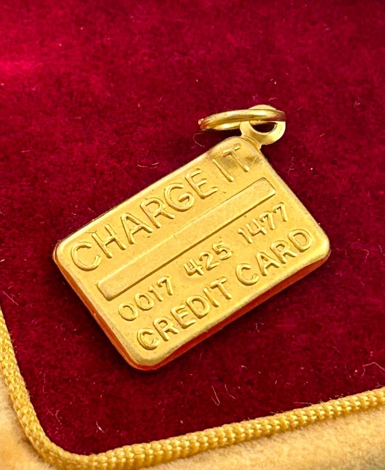 May include: Gold-coloured charm shaped like a credit card with the words "CHARGE IT" and "CREDIT CARD" and the number "0017 425 1477" on it.