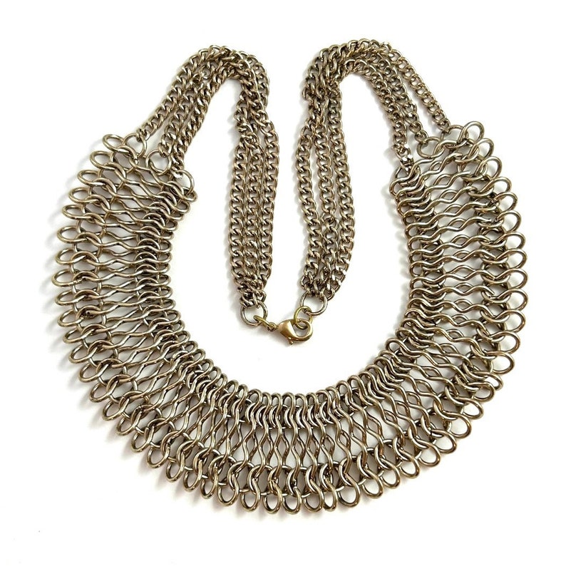 May include: A gold-toned metal chain necklace with a large, intricate, woven design. The necklace is a statement piece and has a clasp closure.