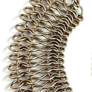 May include: A gold-toned metal chain necklace with a unique, woven design. The chain is made of multiple interconnected loops, creating a textured and intricate pattern.