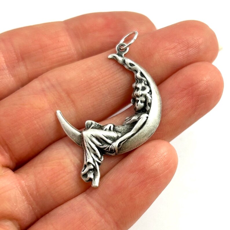 May include: A silver charm pendant featuring a woman sleeping on a crescent moon. The charm is detailed and has a vintage style.