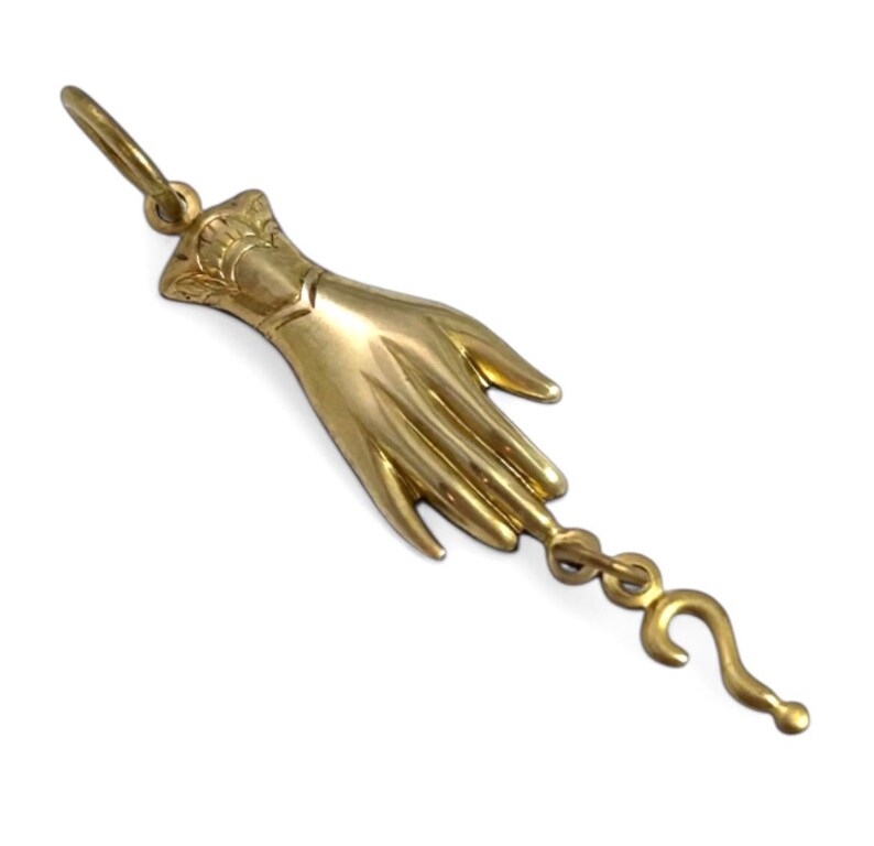 K&ouml;nnte beinhalten: Ein goldfarbener Anh&auml;nger in Form einer Hand mit einem Fragezeichen am Finger.