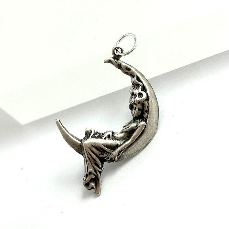 May include: A silver charm pendant featuring a woman sitting on a crescent moon.