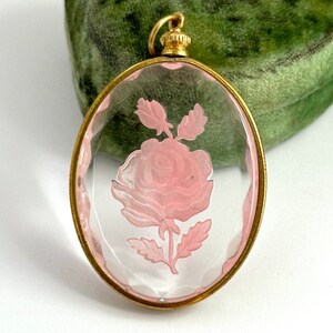 May include: A vintage glass pendant with a gold-tone frame and a pink rose etched inside. The pendant is oval-shaped and has a delicate design.