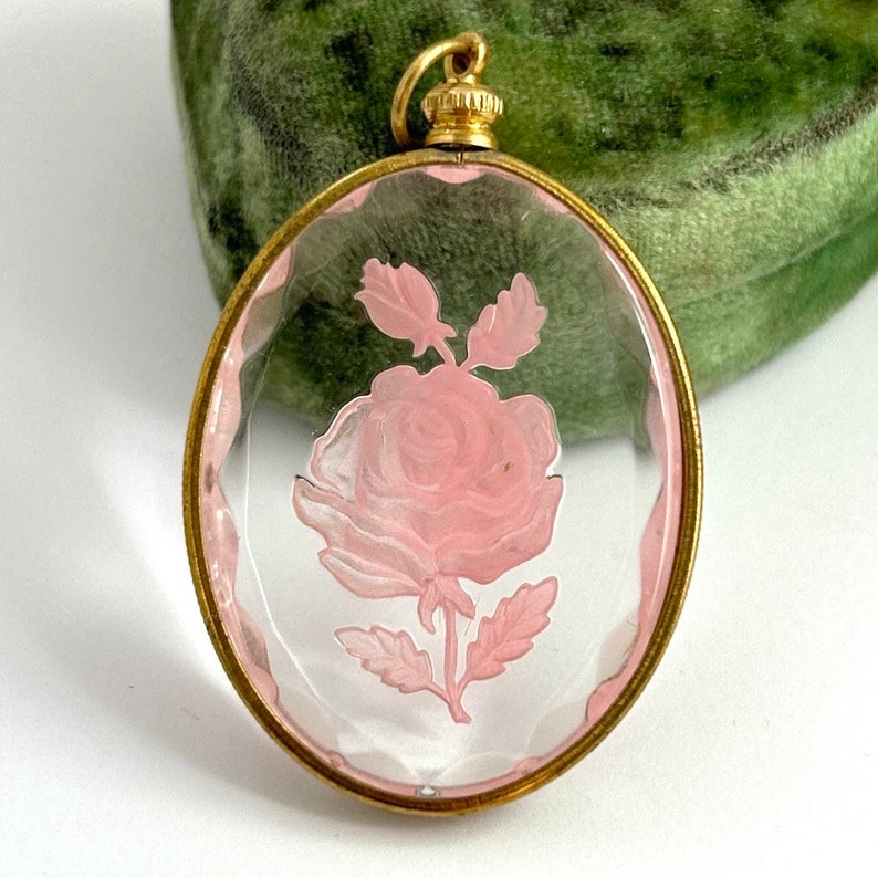 May include: A vintage glass pendant with a gold-tone frame and a pink rose etched inside. The pendant is oval-shaped and has a delicate design.