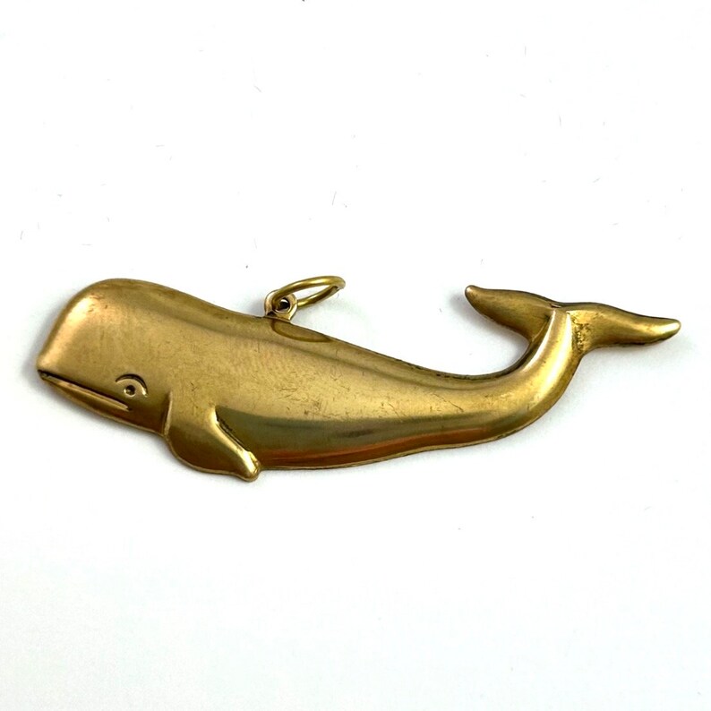 May include: A gold-coloured whale charm pendant. The whale is depicted in a realistic style with a detailed body and tail.