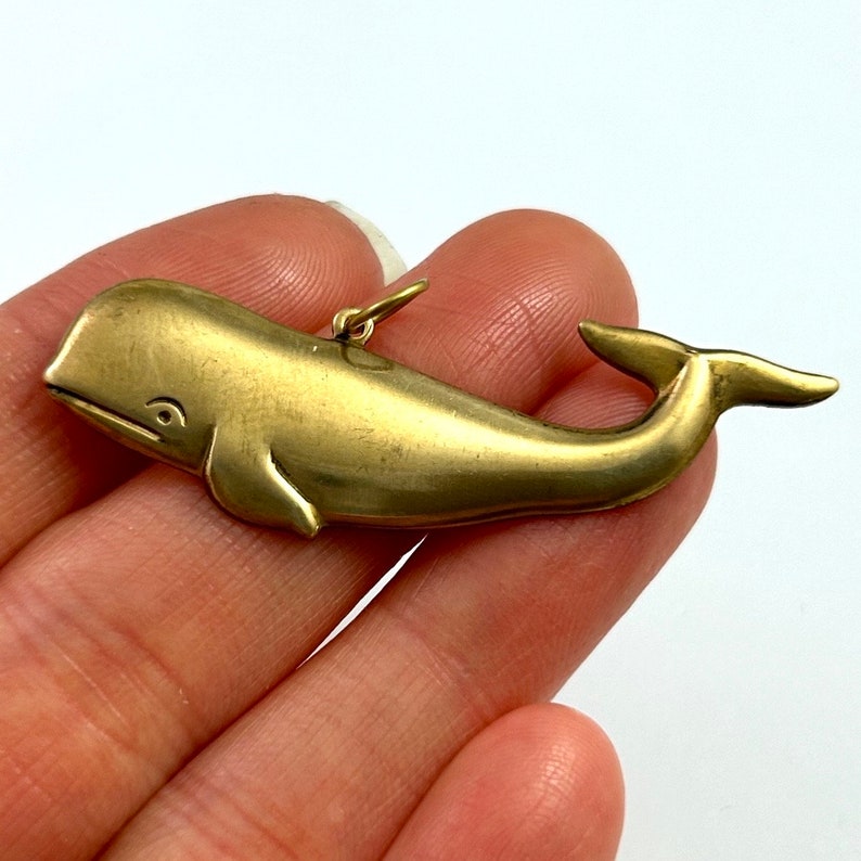 May include: A gold-coloured whale charm pendant. The whale is depicted in a simple, stylised design with a rounded body and a curved tail.