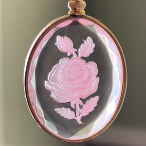 May include: A gold-tone pendant with a clear oval cameo featuring a pink rose etched into the glass.