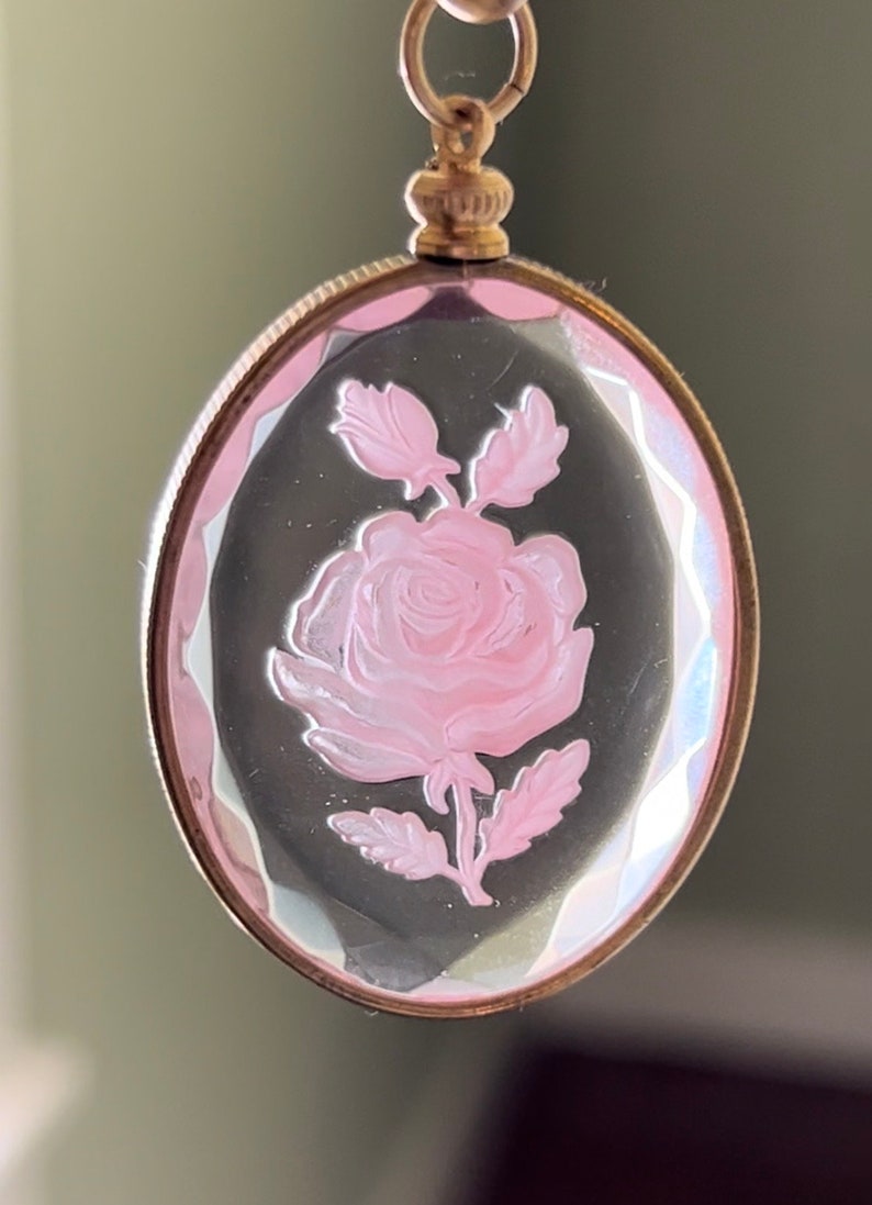 May include: A gold-tone pendant with a clear oval cameo featuring a pink rose etched into the glass.