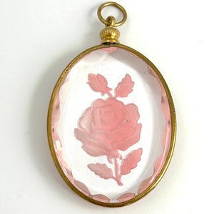 May include: A gold-toned oval locket with a clear glass front featuring a pink rose etched into the glass.