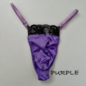 May include: A purple satin thong with black lace detailing at the top. The thong has thin, adjustable straps and the word "PURPLE" is printed in black on the bottom right.