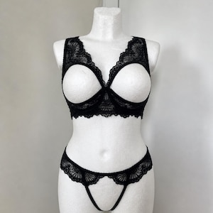 May include: Black lace lingerie set displayed on a white mannequin. The set includes a bralette with open cups and a matching thong. The bralette and thong feature intricate floral lace detailing.