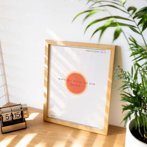 Könnte beinhalten: Ein gerahmter Druck mit einem Holzrahmen und weißem Hintergrund. Der Druck zeigt den Text "PROVERBS 10:5" und "MAKE HAY WHILE THE SUN SHINES." mit einem roten Kreis in der Mitte. Der Druck liegt auf einem Holzregal mit einer kleinen Uhr und einer Topfpflanze.