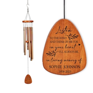 May include: A wooden wind chime with bronze-colored tubes and a wooden plaque. The plaque has the inscription "Listen to the wind and think of me for in your heart I'll always be, in loving memory of Sophie Johnson 1958-2023."