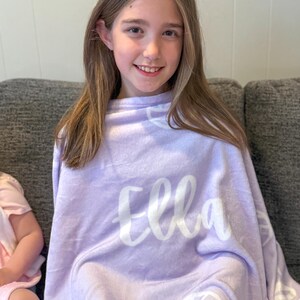 May include: A purple fleece blanket with the name "Ella" written in white cursive lettering. The blanket has a white volleyball design repeated throughout.