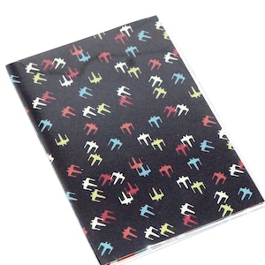 May include: A black notebook with a repeating pattern of colorful X-wing starfighters. The notebook is closed and lying on a white surface.