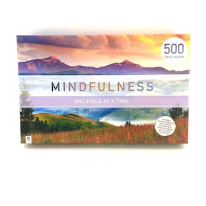 May include: A rectangular jigsaw puzzle box with a landscape image of mountains and fields. The box reads "MINDFULNESS" and "ONE PIECE AT A TIME" with a "500 PIECE JIGSAW" label. The box has a white background.