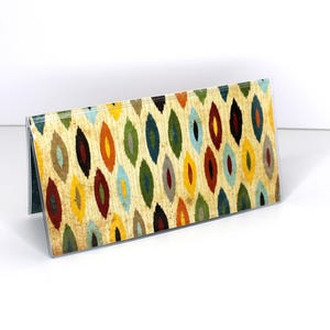 May include: A triangular table top card holder with a colorful abstract pattern of teardrop shapes in shades of red, orange, yellow, green, blue, and brown. The pattern is on a cream background.