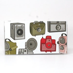 May include: A collection of vintage cameras in various colors and styles, including a red camera with a flash, a green camera with a lens, and a black and white camera with a viewfinder.