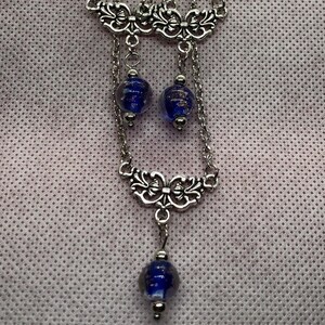 Op de afbeelding: Zilveren kettingoorbellen met blauwe glazen kralen en decoratieve zilveren accenten.