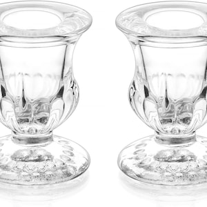 May include: Two clear glass candle holders. Each holder has a round base, a decorative, bulbous body, and a flared top. The glass is transparent, allowing light to pass through. The design is classic and elegant.
