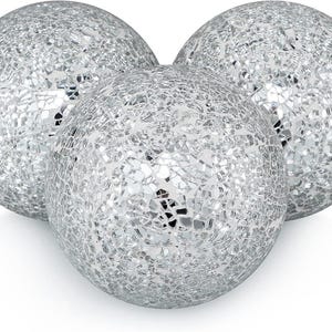 May include: Three decorative silver mosaic spheres. Each sphere is covered in small, reflective pieces, creating a textured, shimmering surface. The spheres are arranged in a cluster, with one in front and two behind.