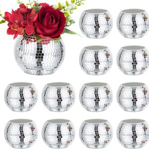 May include: A collection of silver mosaic glass candle holders. One holder contains red flowers. The spherical holders are made of small, reflective tiles. The arrangement includes a vase with flowers and several individual candle holders.