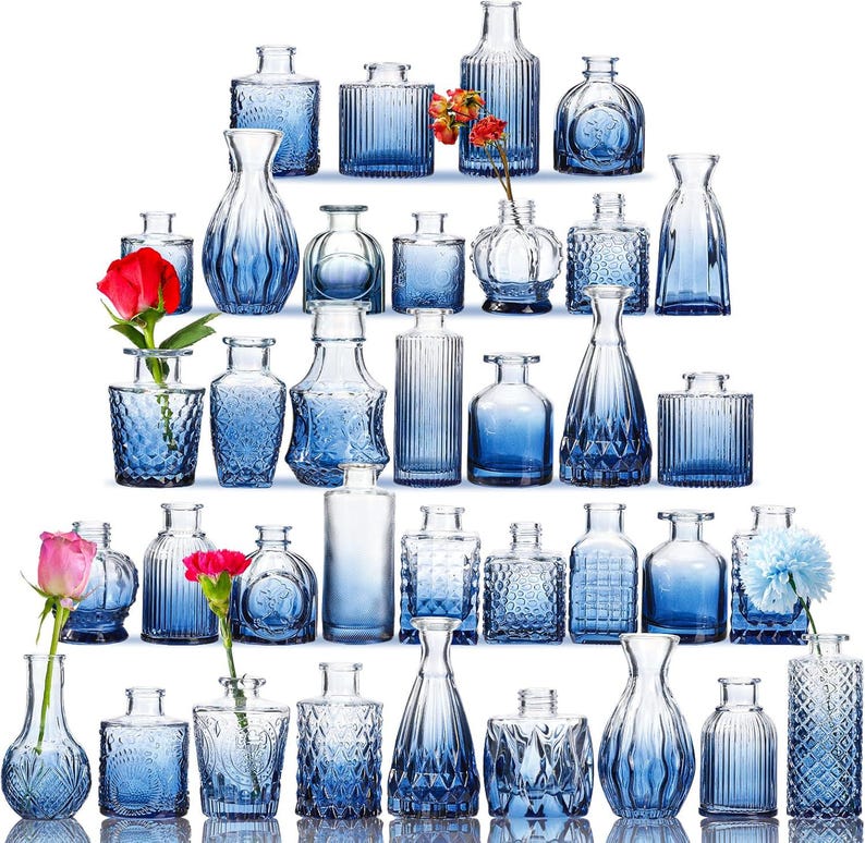 Puede incluir: Colecci&oacute;n de varios jarrones de vidrio azul de diferentes formas y tama&ntilde;os. Algunos jarrones tienen patrones texturizados, mientras que otros son lisos. Varios jarrones contienen flores coloridas, agregando un contraste vibrante al vidrio azul.